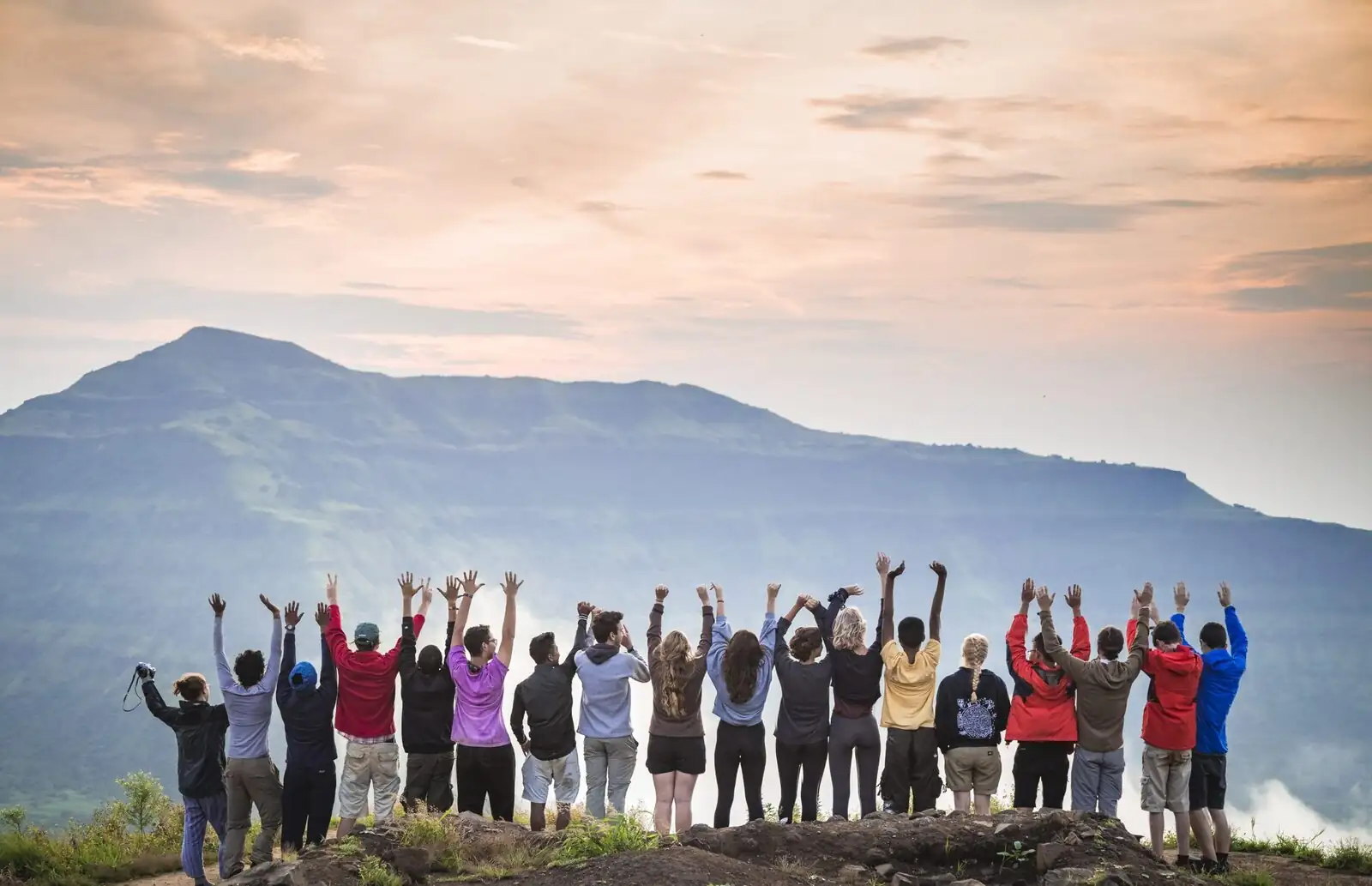 Students with arms raised on a hilltop at sunset